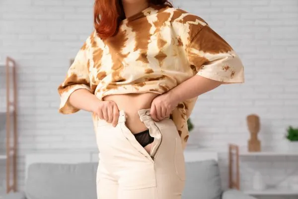Image of woman trying to do her trousers up after pregnancy weight gain Sonning