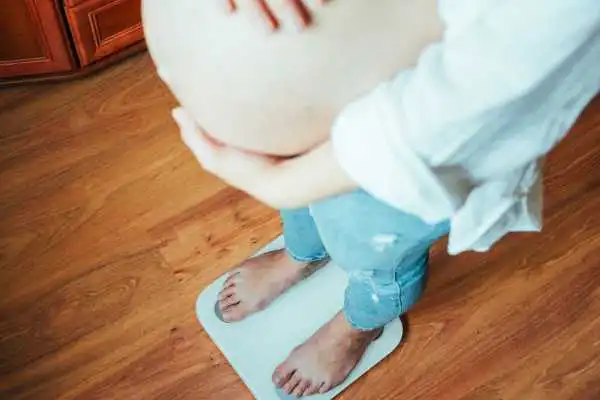 Image of woman weighing herself and experiencing weight gain through pregnancy Sonning